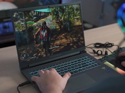 A person playing game on a gaming laptop while using RGB headphones