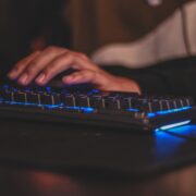 person hand placed on a wired gaming keybaord with blue rgb lights on