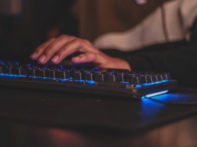 person hand placed on a wired gaming keybaord with blue rgb lights on